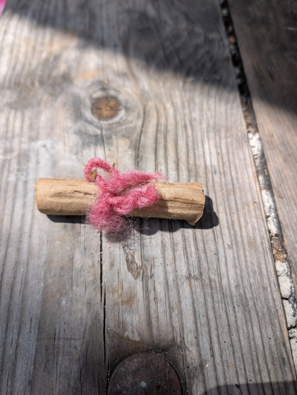 Pink string tied around a wooden stick on a wooden surface